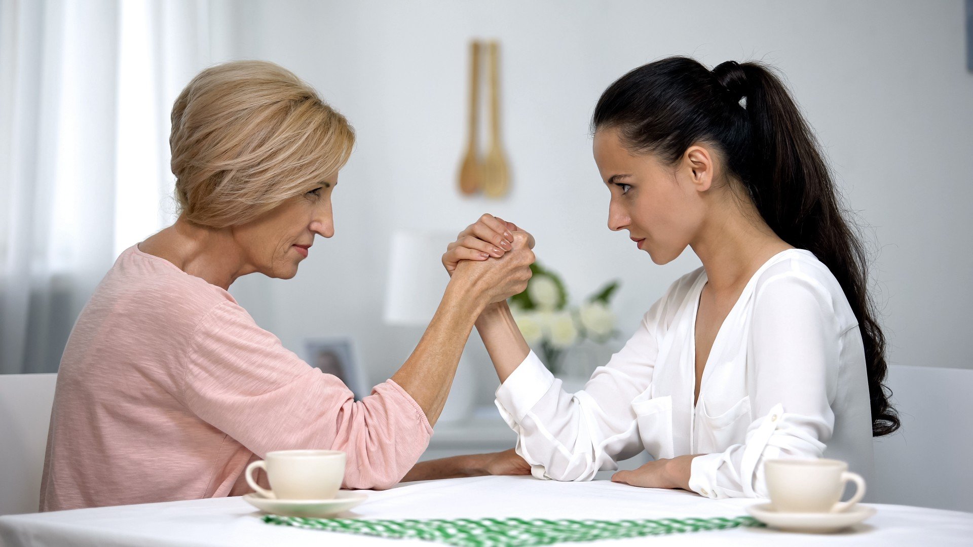 Older woman arm-wrestles a younger woman on wooden table
